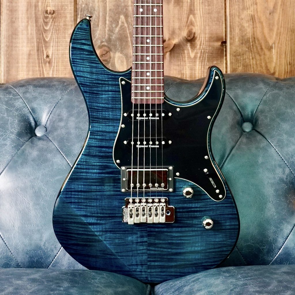Pacifica-1900. Closeup of body of a blue electric guitar propped up on a blue leather couch.