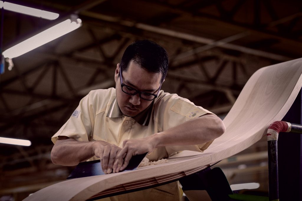 making-a-piano-woodwork Man carving piece of a piano.