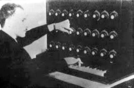 Audion-piano Vintage image of man in suit using the Audion Piano. which look like several rows of dials above a small piano keyboard.