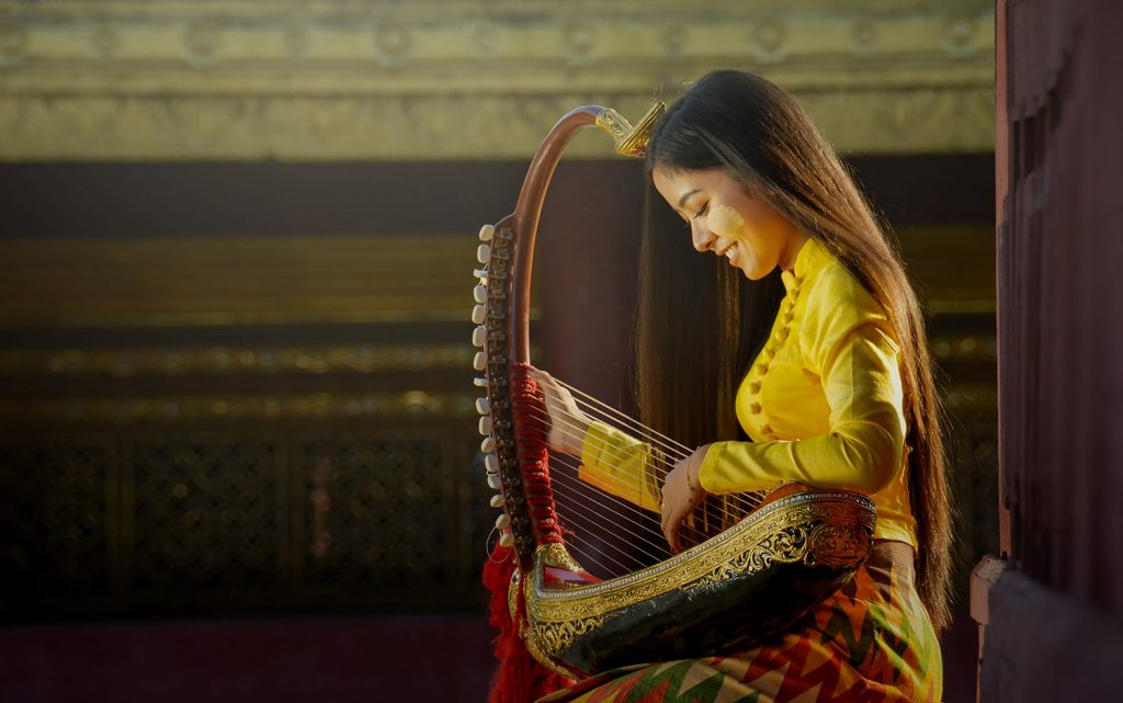 Saung Young woman seen in profile playing a stringed instrument.