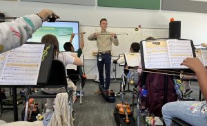 Music educator Tanner Otto showing students how to hold a bow