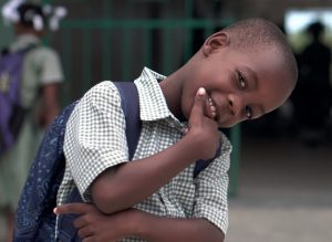 happy Black elementary student standing in front of school gates