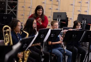 music educator holding flute and overseeing winds ensemble 