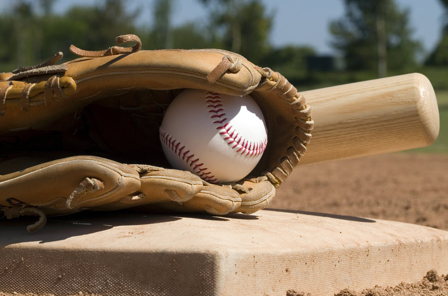 Baseball in glove on a base with a bat next to it.