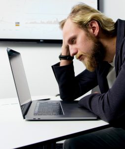 overwhelmed man sitting at desk with open laptop