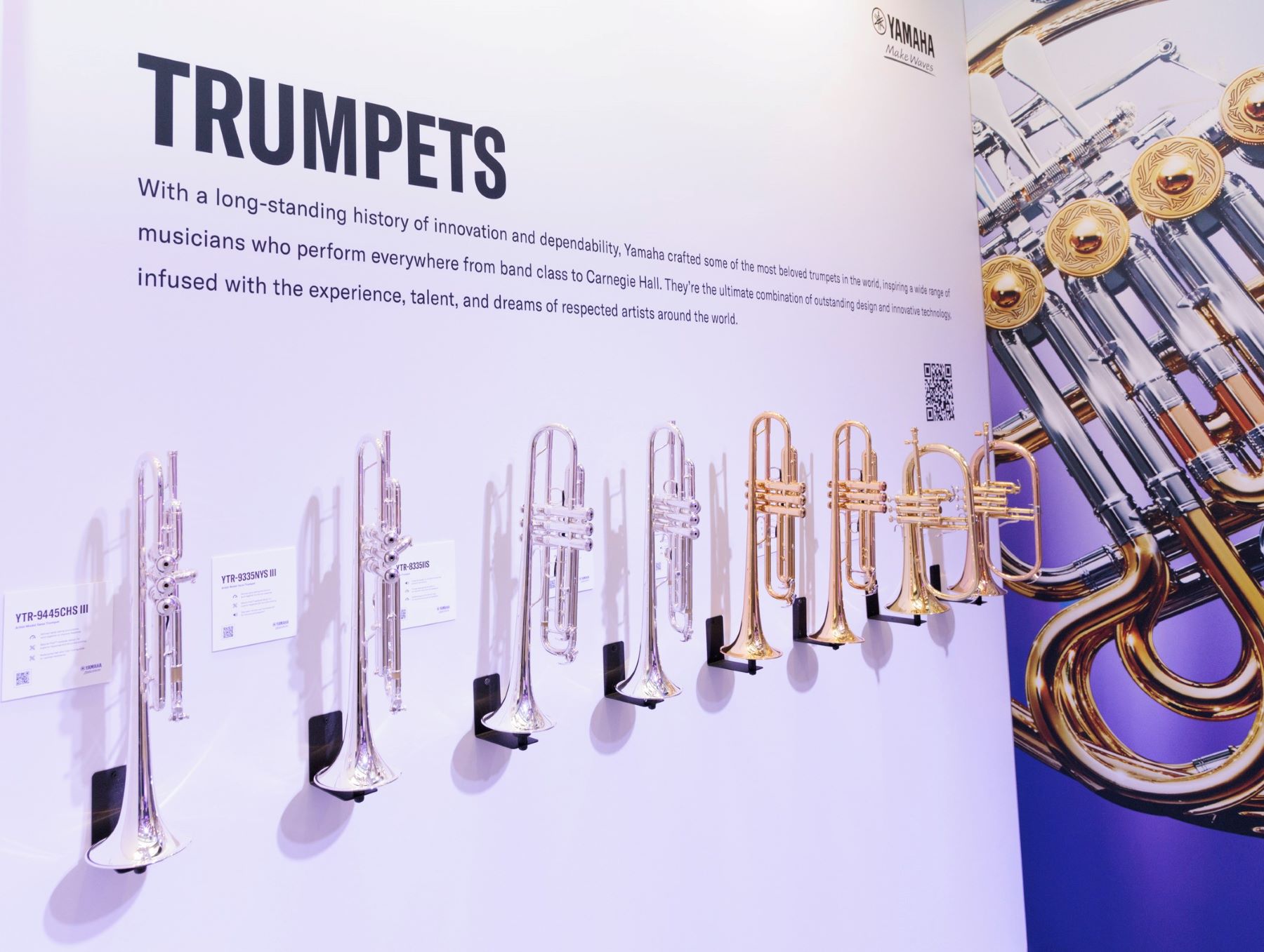 NAMM-2023-Recap-body-image-4 Wall panel with "Trumpets" sign and instruments hanging.