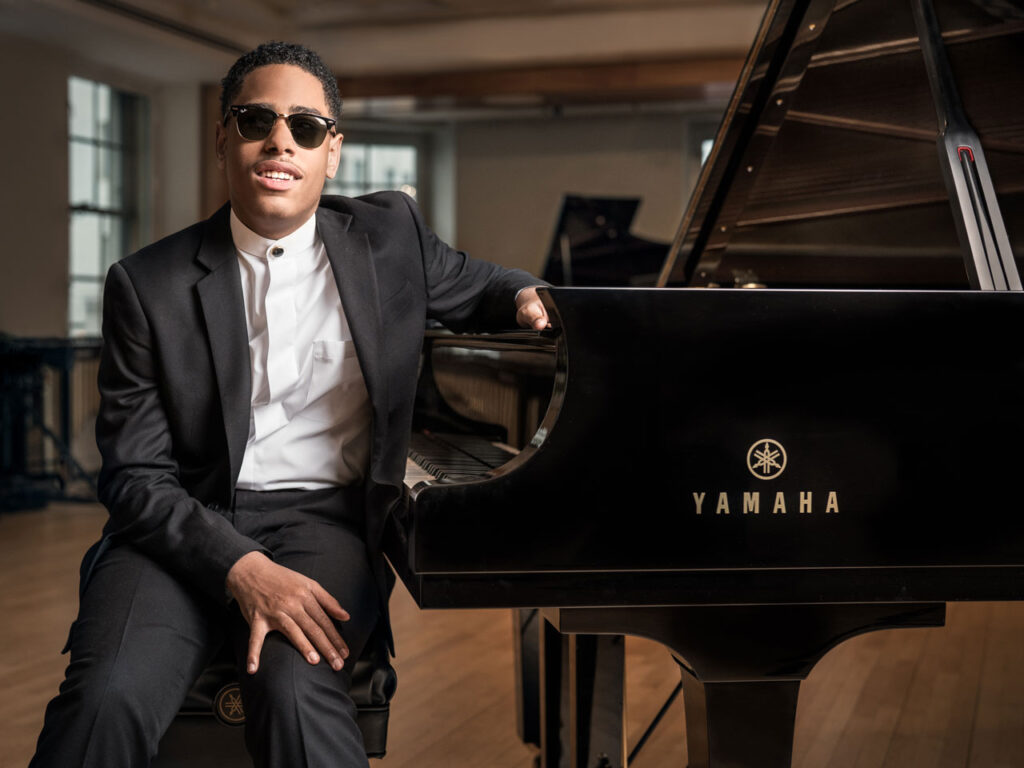 Man smiling for camera sitting at a Yamaha grand piano.