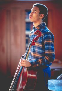 male student standing holding cello