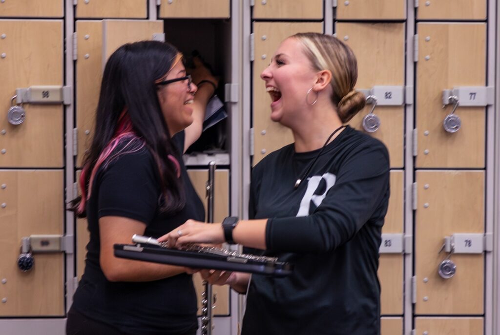 two happy band students talking next to lockers