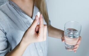 close up of person taking a pill and holding a glass of water