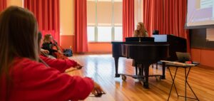 music educator sitting at piano while facing student playing strings instruments