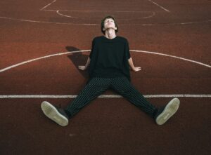 young man sitting on basketball court, looking up and taking a deep breath