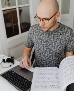 male teacher looking at score while working on laptop