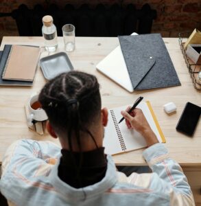 view from behind of someone writing in notebook while seated at a table