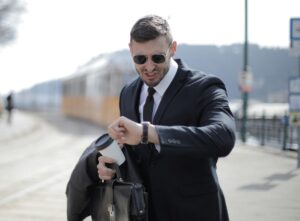 man looking at watch and holding his coat, work bag and coffee cup