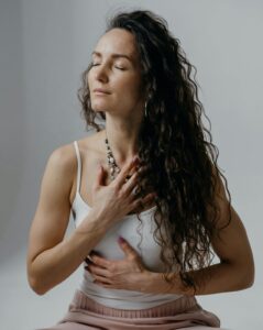 calm woman sitting with one hand on stomach and the other over heart 