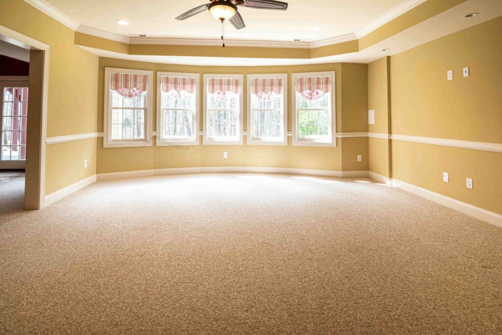A large room with wall-to-wall carpeting and extensive bay windows.